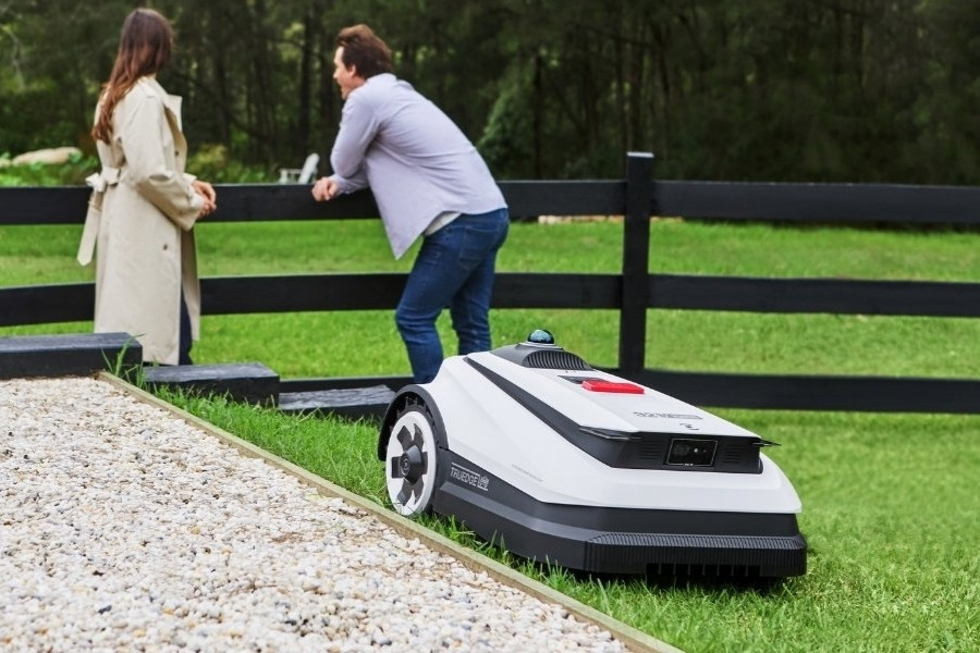 goat maehroboter maht den rasen neben einem sich unterhaltenden paar