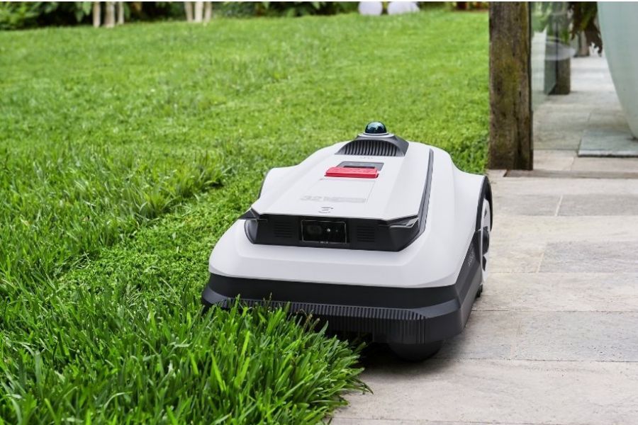 tondeuse à gazon robotisée en forme de chèvre coupant le bord entre l'herbe et le carrelage