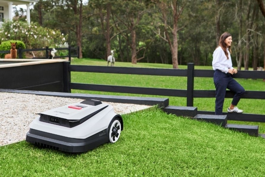 Des robots tondeuses à chèvres tondent un grand jardin devant un couple