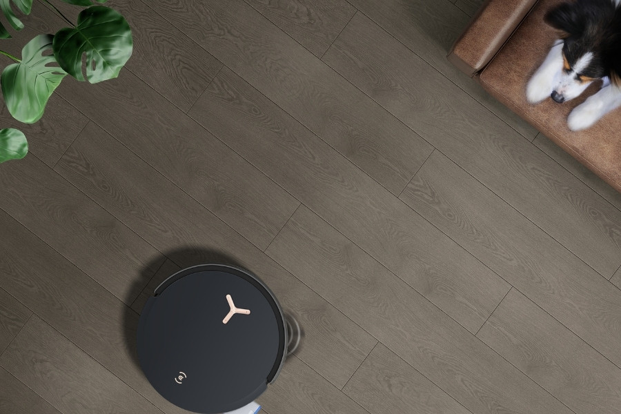 deebot robot vacuum cleaning pet hair on wooden floor while dog watches from couch