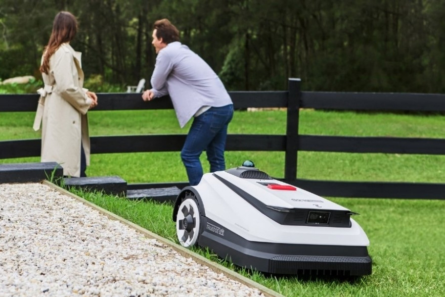 goat robot lawn mower mowing in front of a couple