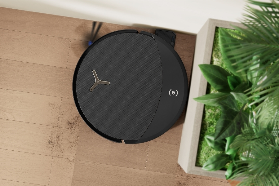 deebot robot vacuum cleaning corner next to a plant pot